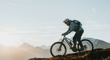Ein Radfahrer bei der Abfahrt mit verschneiten Bergen im HIntergrund | © TVB Wipptal | Johannes Bitter