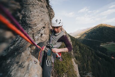 eine Sportlerin hängt am Seil in einer Felswand und hantiert mit einer Expressschlinge | © TVB Wipptal | Johannes Bitter