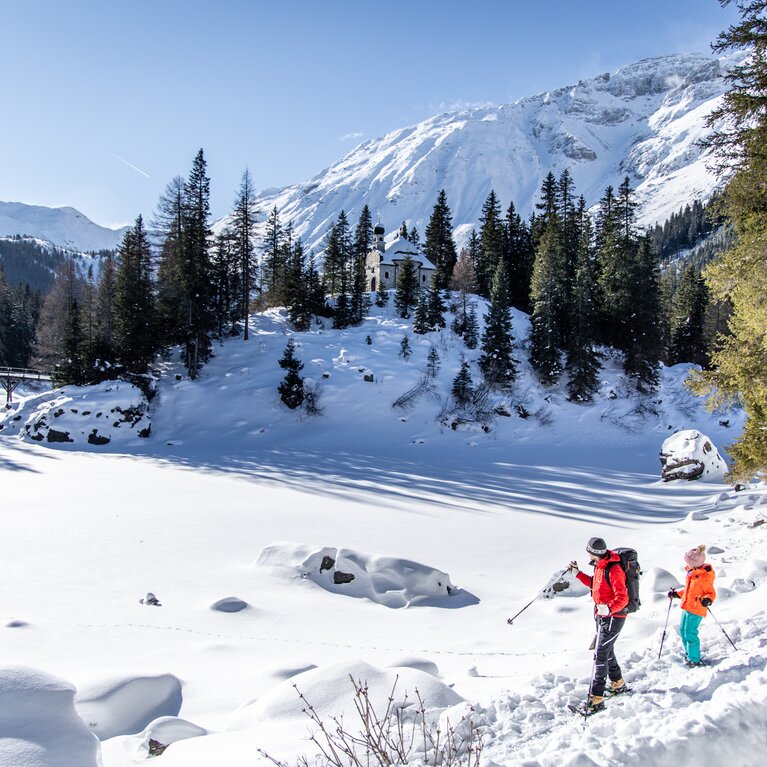 Mann mit Kind geht mit Schneeschuhen am Rand des Sees. | © Ewelina Wild